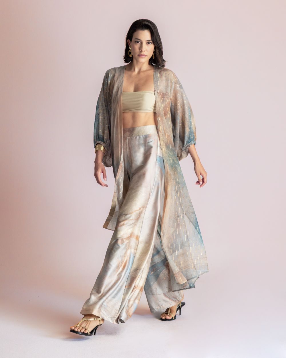 Woman modeling a flowing pastel-print ensemble: loose kimono-style robe over a beige bandeau and wide-leg tie-dye pants, wearing heeled sandals.