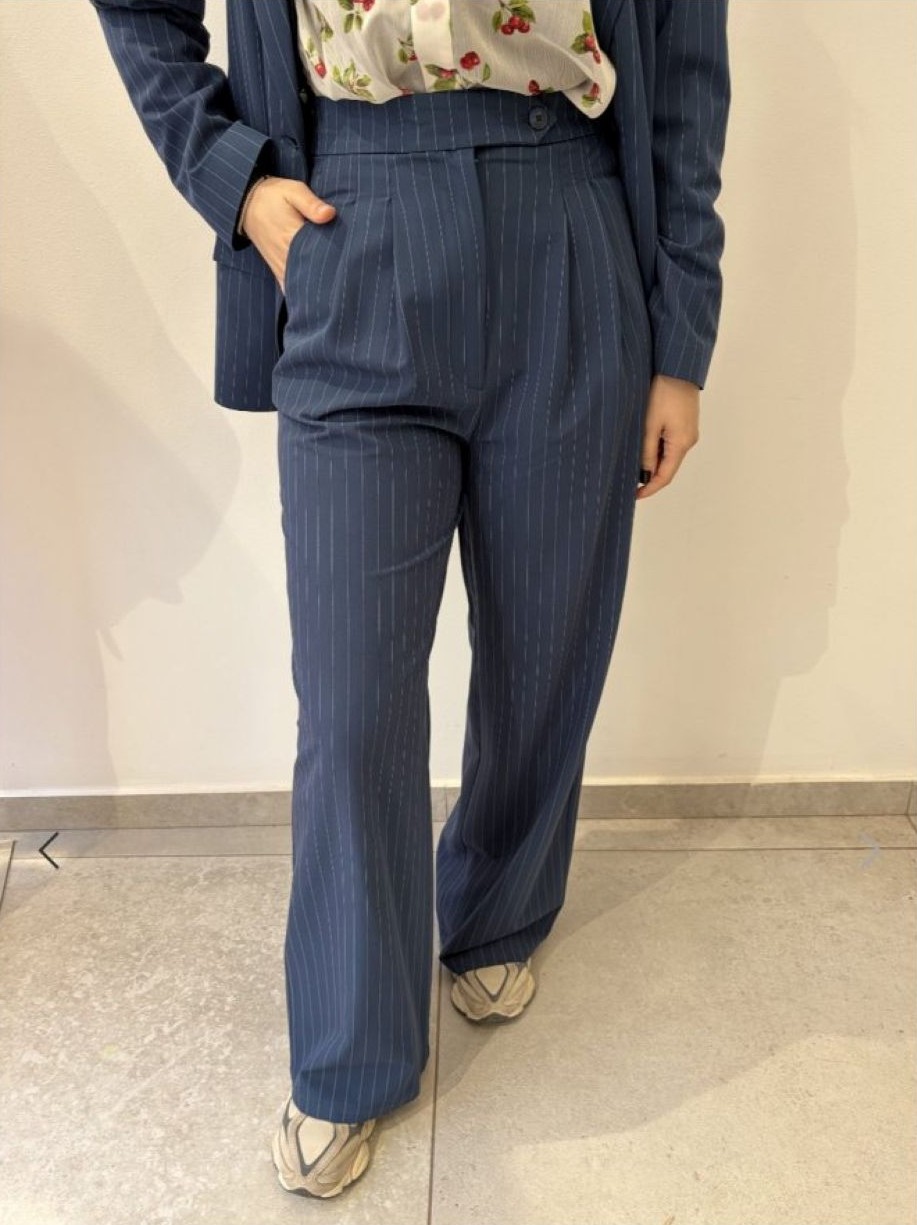 Woman wearing a navy pinstripe blazer and wide-leg trousers with a floral blouse, hands in pockets at the sides.