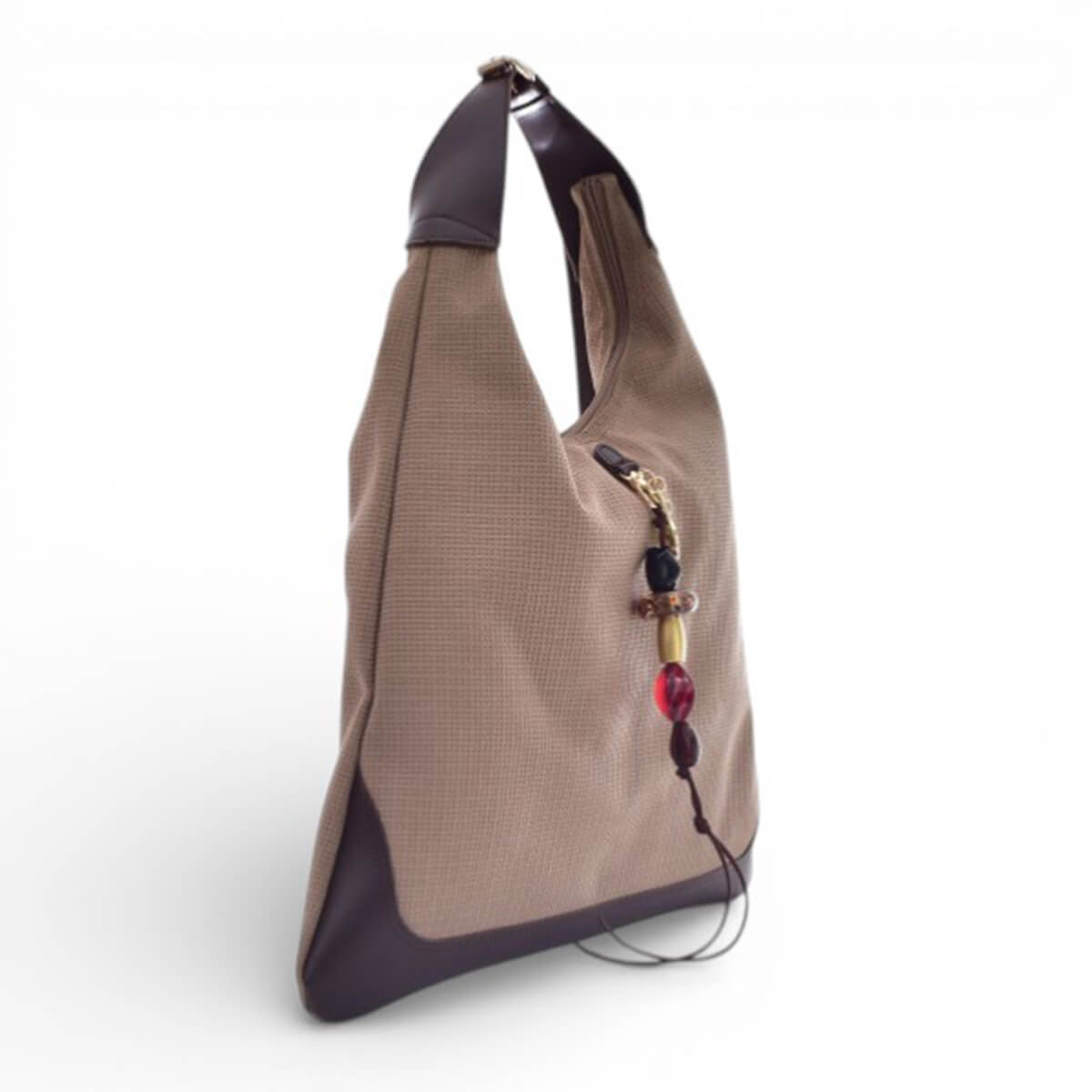 Tan fabric tote bag with dark brown leather base and handles, adorned with a colorful beaded charm.