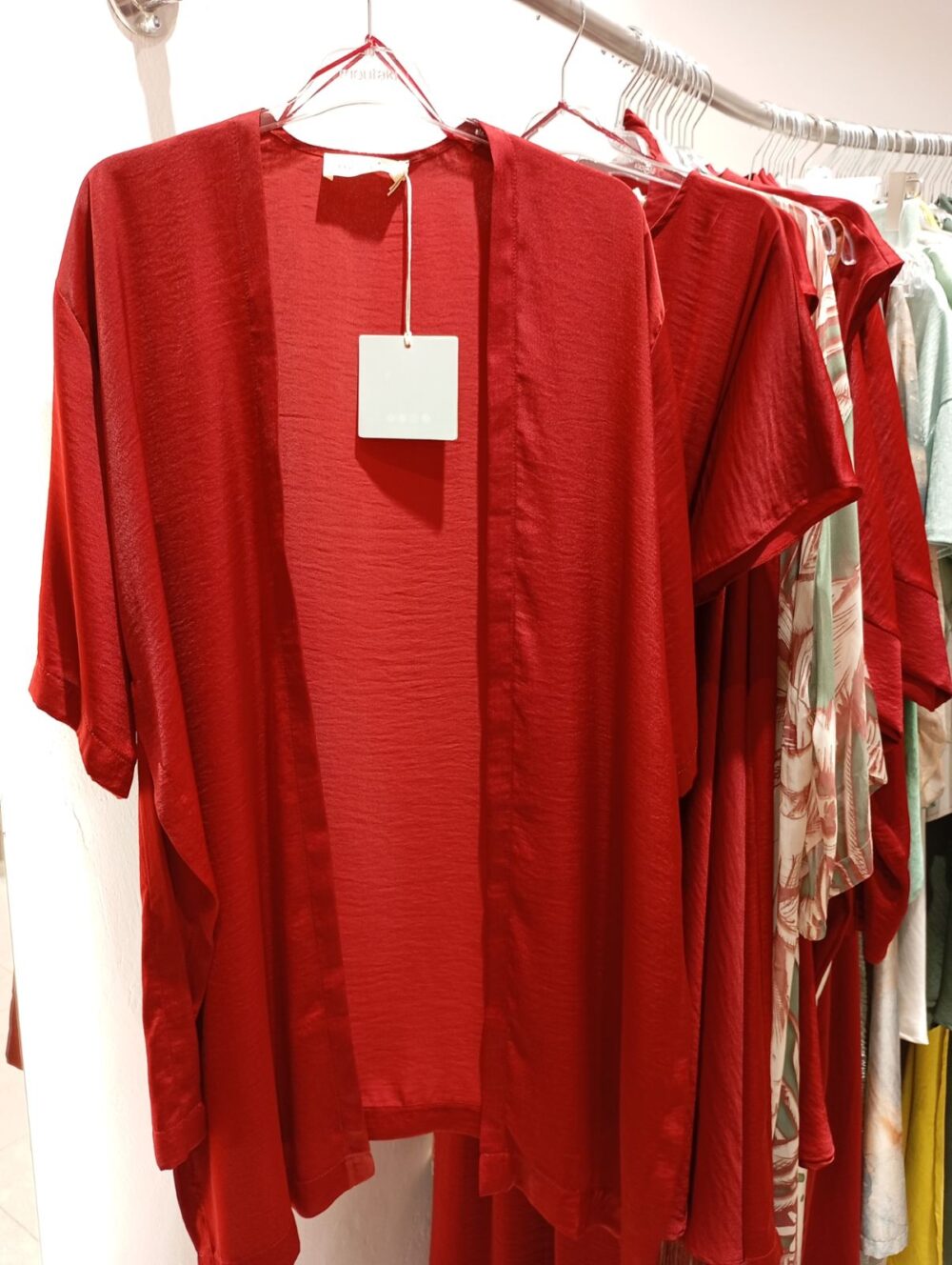 Red flowy garment (dress/top) on a hanger with a white price tag in a store.