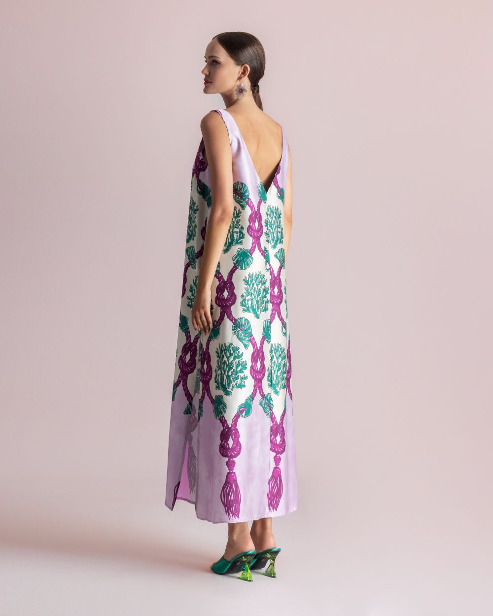 Model wearing a lavender, sleeveless, floor-length dress with green and magenta botanical print, shown from the side/back view.