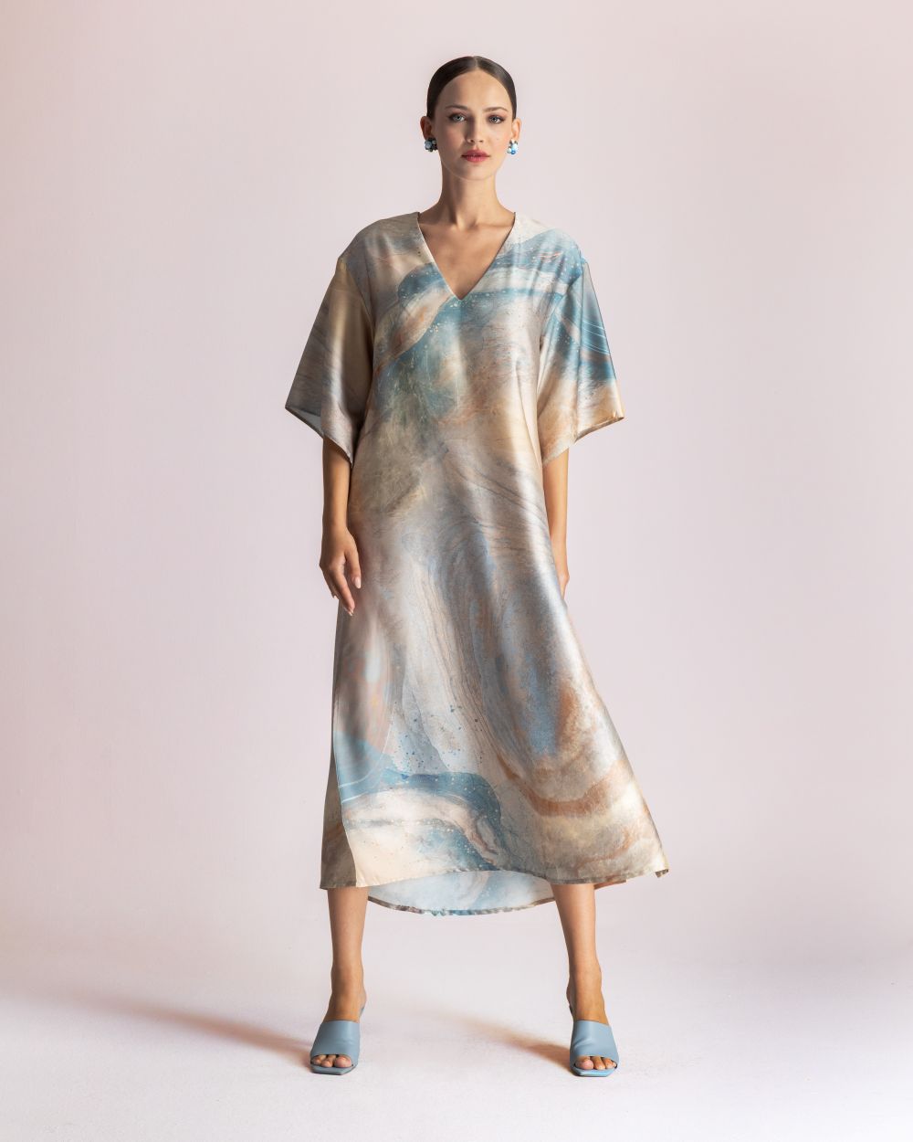 Model wearing a loose, V-neck, pastel tie-dye midi dress with short sleeves and light blue heeled sandals.