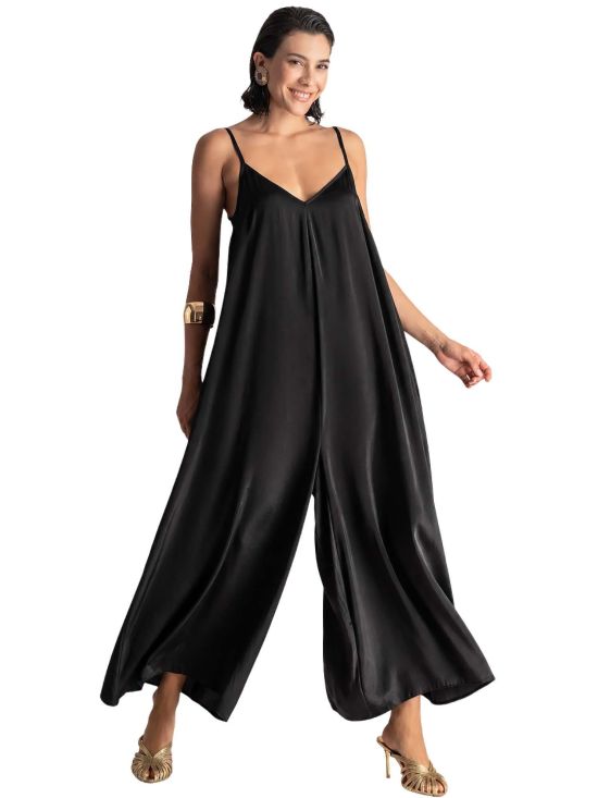 Woman wearing a black satin wide-leg jumpsuit with thin spaghetti straps and a V-neckline, posing smilingly.