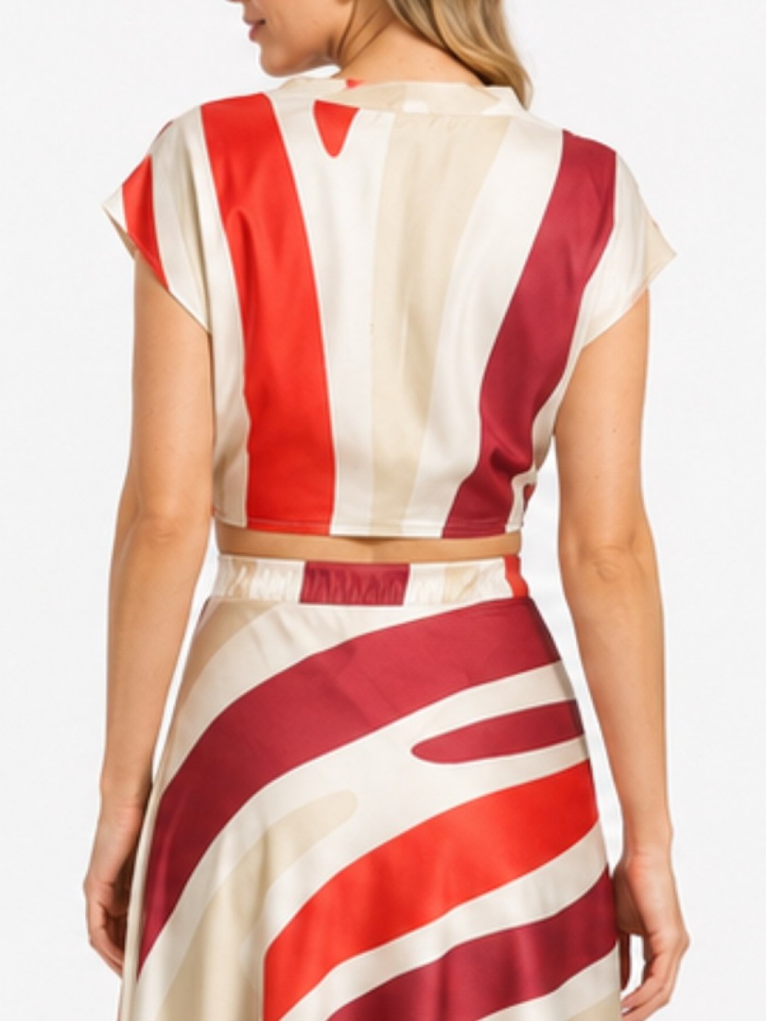 Back view of a woman wearing a sleeveless striped dress with red, cream, and maroon diagonal and vertical patterns, tied at the waist with a beige belt.