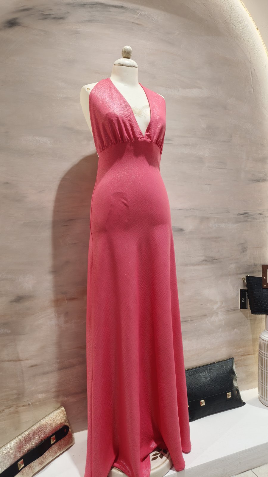 Pink floor-length halter dress on a mannequin in a boutique display window, with a gathered waist and flowing skirt.