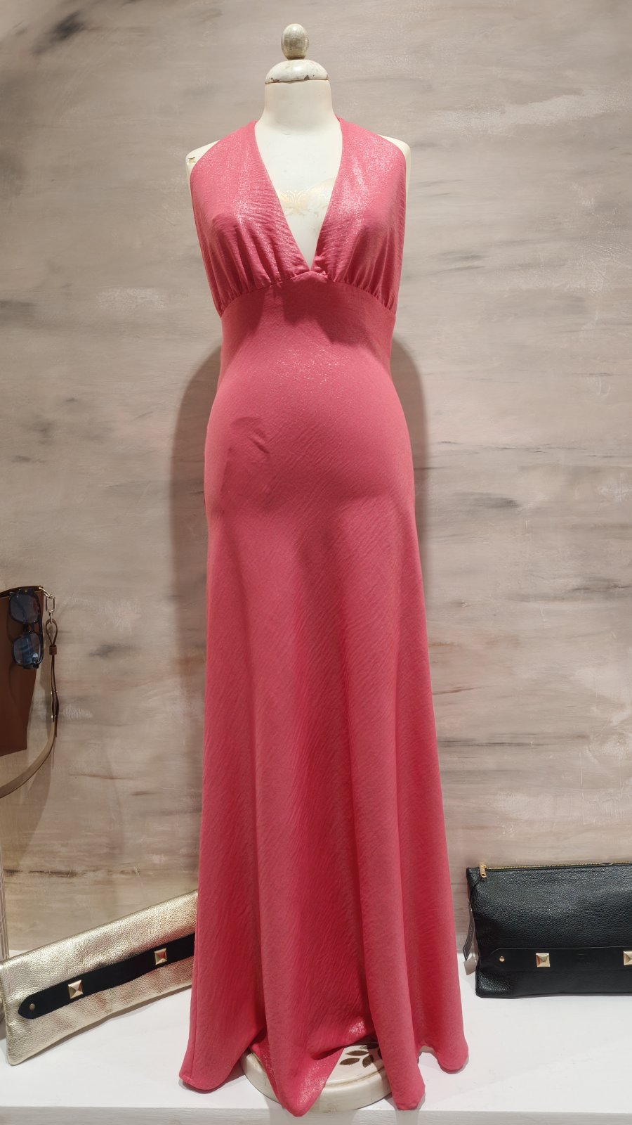 Pink halter-neck maxi dress on a mannequin in a store display against a beige wall.