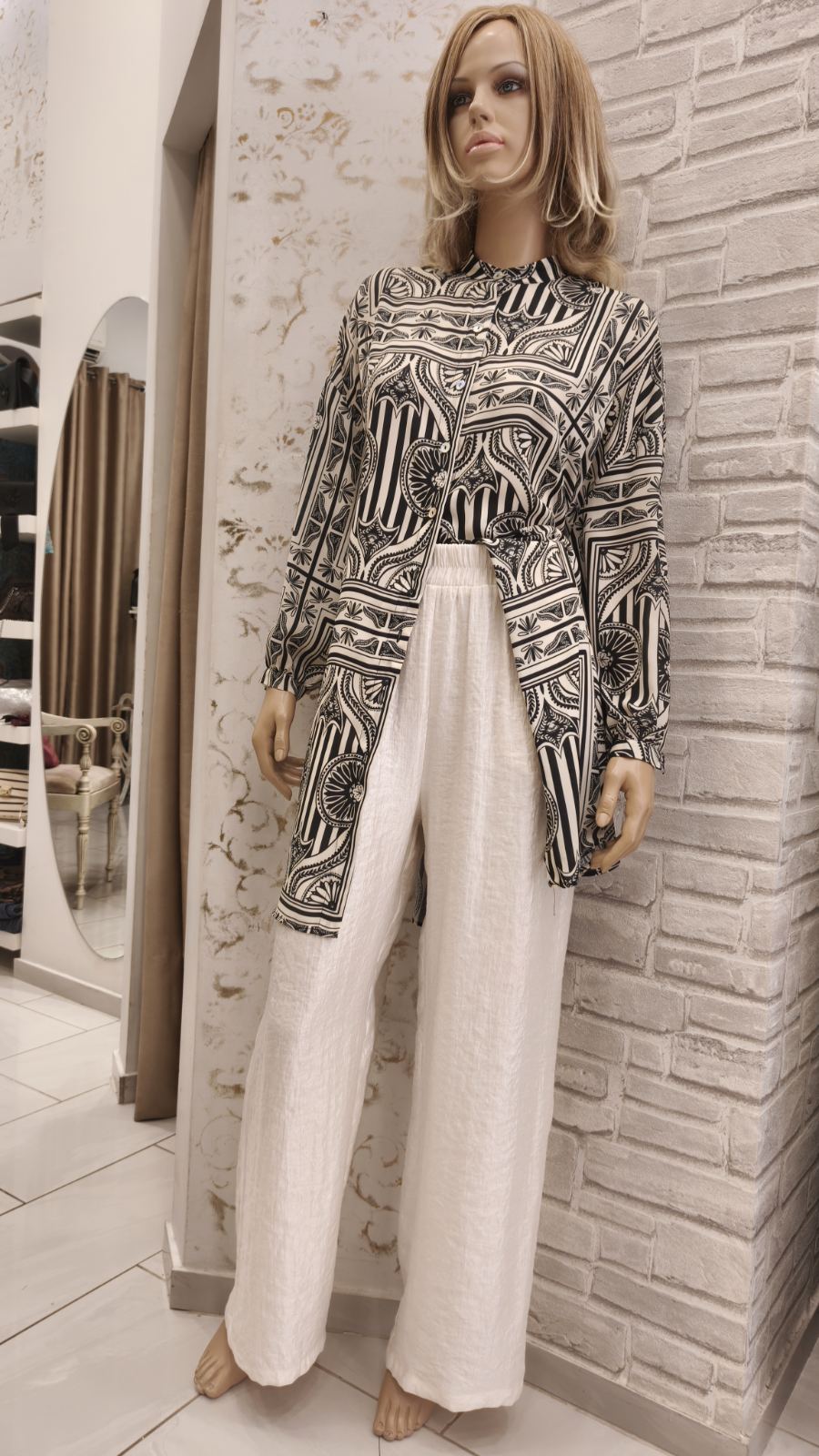 Mannequin wearing a black-and-white geometric patterned long-sleeve tunic over white wide-leg pants in a boutique store